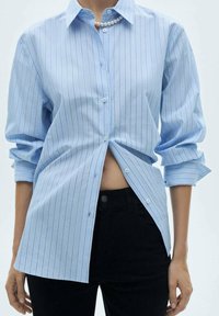 Lichtblauw gestreept button-up shirt met een kraag, voorzien van opgerolde mouwen en een net iets relaxte pasvorm, gecombineerd met zwarte broek.