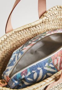 Sac en paille tissé avec des poignées en cuir marron clair. Contient une pochette intérieure zippée à motif floral dans des couleurs bleu, rouge et vert.