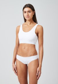 Bralette en coton blanc avec un décolleté en scoop et des larges bretelles, associé à une culotte blanche à bordure en dentelle. Texture lisse, design simple.