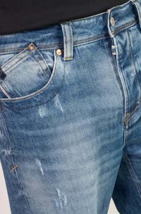 Lichtblauwe denim jeans met versleten details, vijf-pocketontwerp en koperkleurige hardware. Voorzien van contrasterende stiksels langs de tailleband.