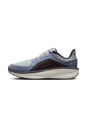 Zapatilla de color azul claro y marrón oscuro con un upper texturizado, suela lisa y detalles reflectantes. Presenta el logotipo de GORE-TEX en el talón.