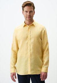 Camicia di lino gialla a maniche lunghe con chiusura a bottoni e colletto a punta; presenta una texture liscia e una vestibilità classica.