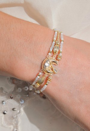 Bracelet en or et en argent avec des perles blanches, des accents texturés et du matériel décoratif. Deux couches avec un design flexible et des pierres précieuses transparentes.