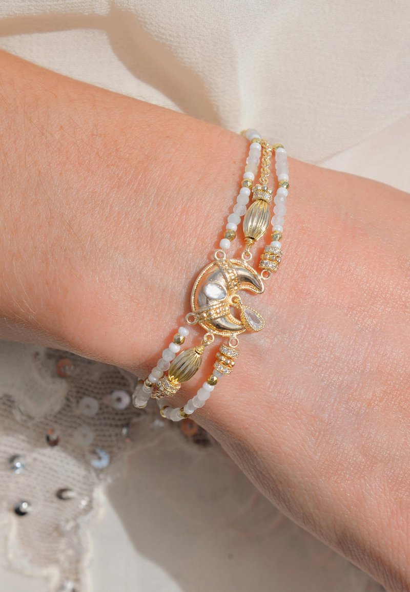 Bracelet en or et en argent avec des perles blanches, des accents texturés et du matériel décoratif. Deux couches avec un design flexible et des pierres précieuses transparentes.