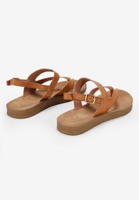 Sandalias de cuero marrón con tiras cruzadas y una hebilla ajustable. Cuenta con una plantilla acolchada y una suela de goma plana y texturizada.