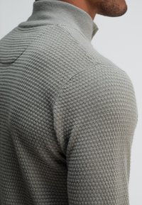 Grijze gebreide trui met een gestructureerd patroon, voorzien van een hoge kraag en raglanmouwen, aansluitend ontwerp.