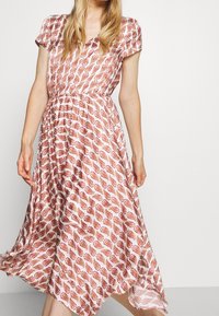 Maxi-jurk met bloemmotief in lichte stof, voorzien van korte mouwen, een geraffineerde taille en een vloeiende silhouet in wit en roodachtige tinten.