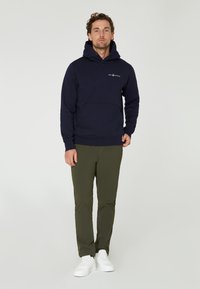 Sudadera con capucha de color azul marino, con un bolsillo frontal, puños acanalados y dobladillo. Combinada con pantalones verde olivo y zapatillas blancas.