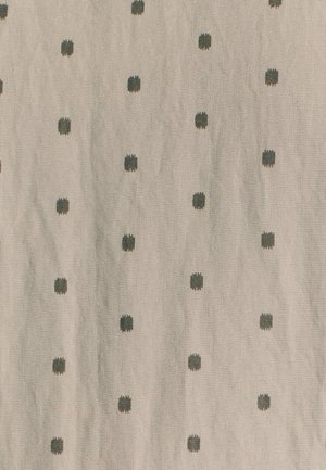 Tissu textile avec un fond beige clair orné de motifs de points verts foncés dispersés, de tailles et de formes variées, avec une finition texturée.