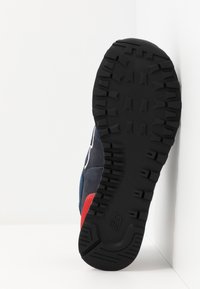 Sole modré tenisky s černým vzorem na podrážce a červeným akcentem na mezipodrážce, umístěná na bílém pozadí v rohu.