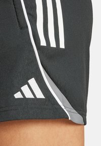 Zwarte sportshorts van lichtgewicht materiaal hebben drie witte verticale strepen en een witte geborduurde logo op de onderste zoom.