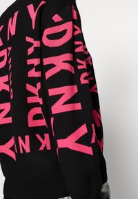 Pull noir en maille avec un motif répétitif de texte "DKNY" en rose, bordure côtelée et encolure ronde.