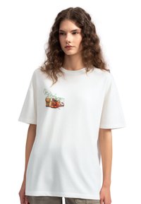 Witte katoenen t-shirt met een losse pasvorm, voorzien van een geprint ontwerp van potten en groenten op de voorkant. Korte mouwen en ronde hals.