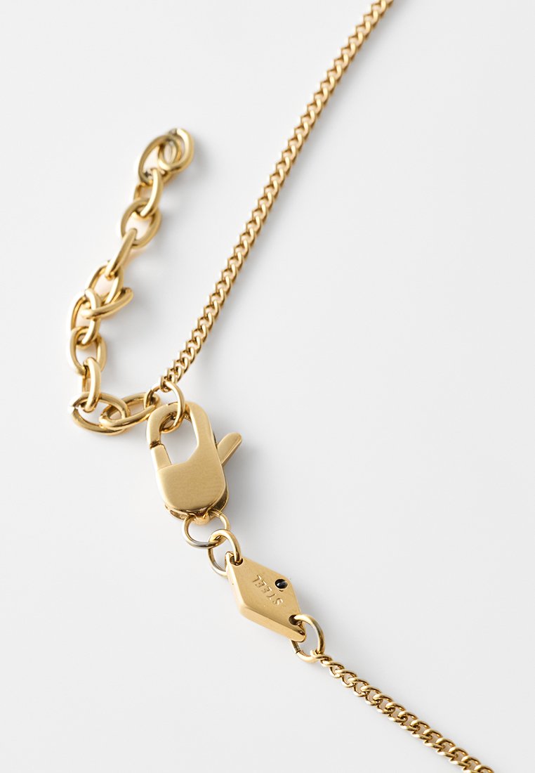 Goldfarbene Metallkette mit einem Verschluss, die aus miteinander verbundenen Gliedern und einer glatten Oberfläche besteht. Bemerkenswerte Details sind ein kleines Etikett mit der Gravur "STELLA".