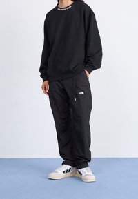 Černá mikina s logem "THE NORTH FACE" na výstřihu, spárovaná s černými kalhotami s detaily loga a nastavitelným pasem; bílé a šedé tenisky.