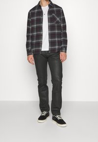Koszula w kratę z flaneli w kolorze czarnym, czerwonym i białym; biała koszulka pod spodem; czarne spodnie slim fit; czarne trampki z białą podeszwą.