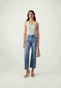 Light gray ribbed tank top, high-waisted light blue jeans with frayed hem, and beige heeled sandals. Holding a small beige handbag.