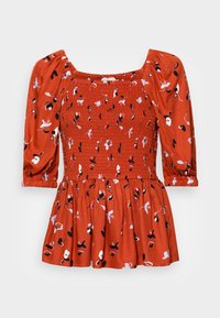 Top floral vermelho com decote quadrado, mangas bufantes e corpete franzido. O tecido apresenta padrões florais em preto e azul claro numa superfície texturizada.