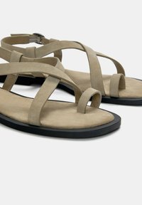 Beige velúr szandálok keresztbe fonott pánttal, állítható boka csattal, fekete gumitalppal és sima, texturált talpbetéttel.