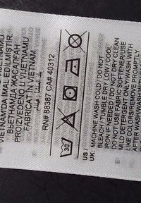 Étiquette d'entretien avec pictogrammes de lavage : lavage à 30°C, pas d'eau de javel, séchage en machine à basse température, repassage doux, ne pas nettoyer à sec, et instructions de lavage détaillées en plusieurs langues.