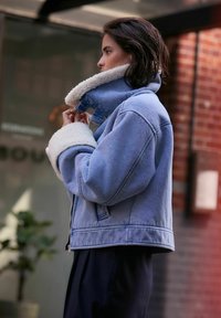 Giubbotto di jeans con una finitura azzurro chiaro, colletto e polsini in shearling bianco, chiusura con zip e tasche laterali, con un taglio rilassato.