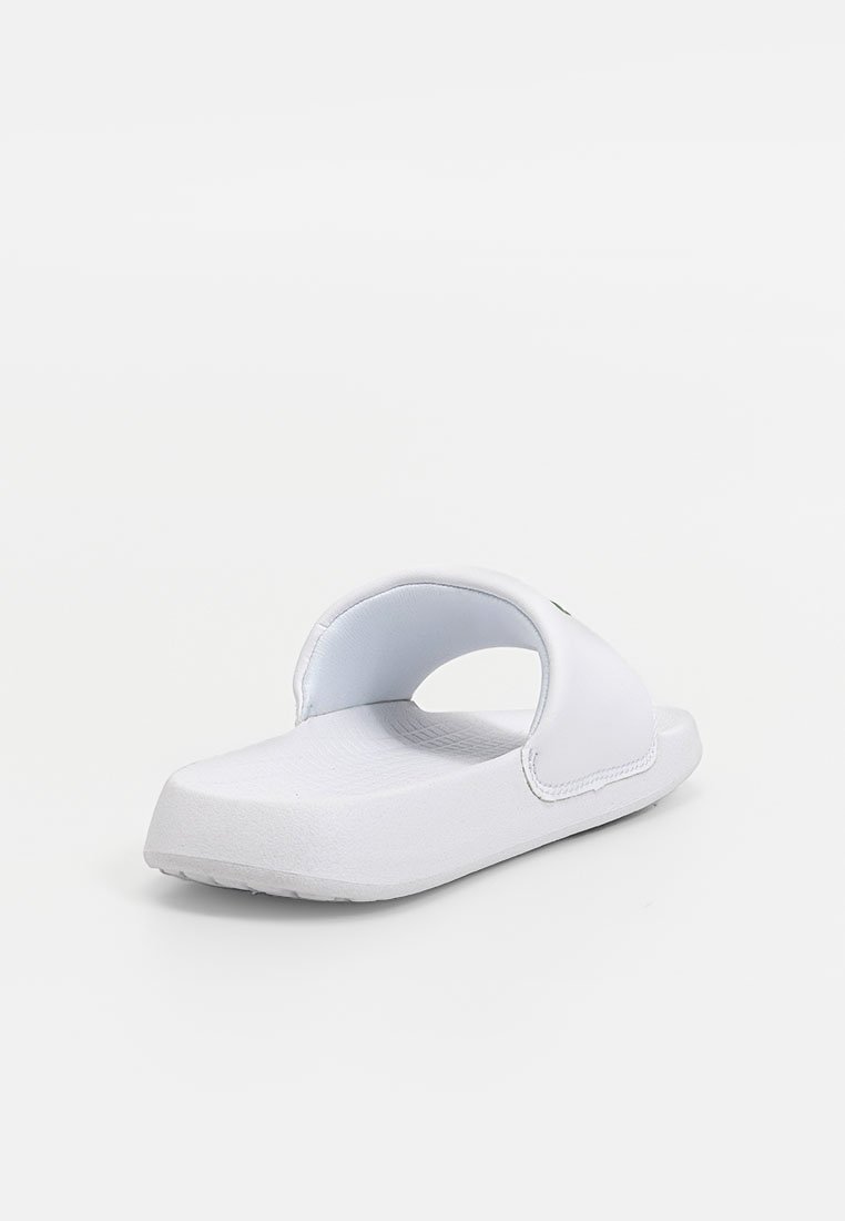 Sandale blanche à semelle plate avec une large bride et un dos ouvert. Fabriquée en matériau lisse avec un semelle texturée.