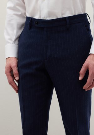 Pantalon rayé bleu marine en tissu texturé, doté d'une fermeture à bouton et de passants pour ceinture. Le design comprend des fines rayures verticales et un devant plat.