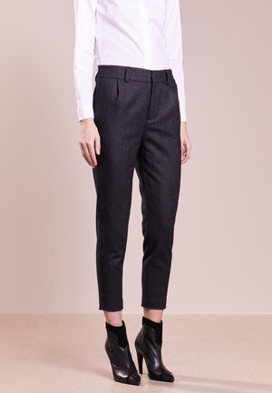 Osoba nosząca dopasowane ciemnoszare spodnie do kostek, białą, długorękawową koszulę włożoną do środka oraz czarne botki na wysokim obcasie.