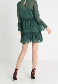 Grön, lager-på-lager klänning med volangärmar och spetsdetaljer. Bärs med bordeauxfärgade högklackade skor. Slät, lättvikts tyg.