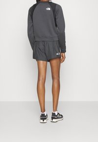 Sudadera deportiva negra con tejido texturizado, con un logo en la parte trasera, combinada con pantalones cortos para correr negros y zapatillas negras y blancas.