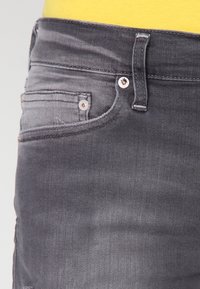 Tmavě šedé džíny z denimu s zipem, standardním designem pěti kapes a kontrastním prošíváním. Hladká textura s mírným opotřebením.