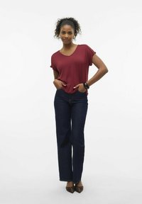 Camiseta corta de manga maroon con escote en V, combinada con jeans de pierna ancha de color azul oscuro. Incluye pulsera negra y zapatos marrones de punta.