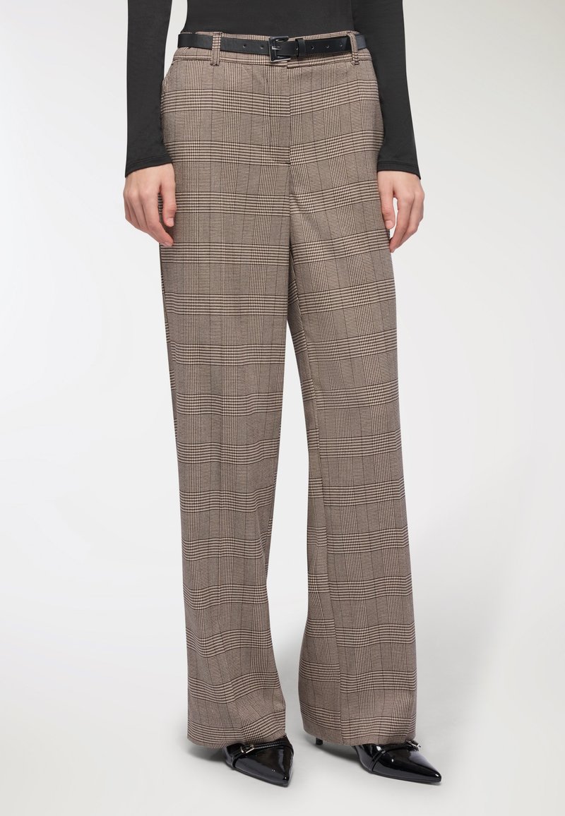 Pantaloni a gamba larga in un motivo a quadri marrone e beige, realizzati in un tessuto texturizzato, con passanti per cintura e indossati con scarpe nere a punta.