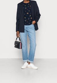 Marineblauwe top met bloemenborduursel, gecombineerd met een marineblauwe blazer en lichtblauwe opgerolde spijkerbroek. Witte sneakers en een kleine zwarte handtas met een rood accent.