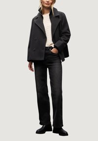 Svart dubbelknäppt kappa med breda slag över en krämfärgad kabelstickad tröja, matchad med svarta raka jeans och svarta ankelstövlar.