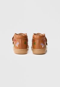Zapatillas altas de cuero marrón con diseños bordados, incluyendo hongos y hojas, y una suela de goma beige. Correas laterales ajustables.