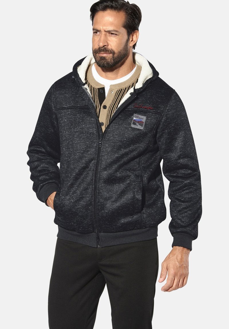 Men's black fleece-lined jacket with a zip closure, ribbed cuffs, front pockets, and a patch featuring a mountain design.