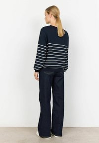 Navy striped long-sleeve top with white horizontal stripes, paired with dark blue flared jeans and white sneakers, viewed from the back.
