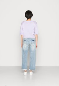 Suéter lilás de malha com mangas curtas, combinado com jeans de perna larga azul claro com bolsos traseiros com desgaste e bainhas desfiadas, completado com sapatilhas brancas.