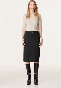 Beige kurzärmliges Oberteil kombiniert mit einem schwarzen Bleistiftrock mit einem dezenten Gürteldetail, ergänzt durch kniehohe schwarze Lederstiefel.