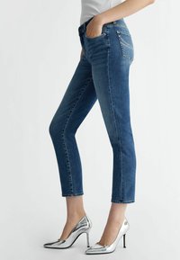 Modri denim skinny jeans s srednjim pasom, ki imajo klasičen dizajn petih žepov in srebrne detajle na zadnjih žepih.