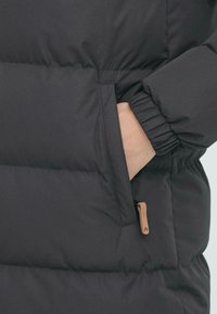 Svart boblejakke med quiltet tekstur, elastiske mansjetter, en sidelomme og en liten tan læderdetalj på glidelåsen.
