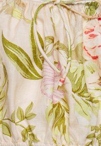 Tissu léger avec un imprimé floral comprenant des feuilles vertes et des fleurs roses, froncé en haut avec un cordon de serrage.