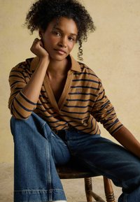 Pruun ja tumesinine triibuline pikakä sleeves polo särk V-kaelusega, sobitatud laia jala siniste teksadega. Mudel toetab lõua käele, isteposti. 