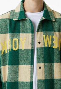 Grüne und cremefarbene karierte Jacke aus Wollmischung, mit Kragen, gelber "NEW YORK" Schriftzug und Druckknopfverschlüssen.