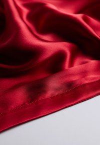 Röd satin tyg med en slät textur, som har en subtil glans och en vikning i kanten. Ytan visar mjuka draperingar och mjuka konturer.