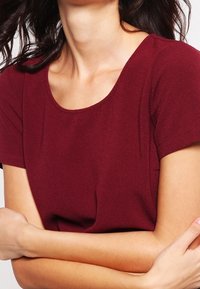 Haut bordeaux à manches courtes avec un col rond, confectionné dans un tissu doux et texturé. Présente une silhouette ajustée et un minimum de détails.