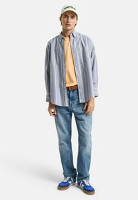 Gestreiftes Hemd in Hellblau, orangefarbenes T-Shirt darunter, blaue Jeans und blaue Wildledersneaker mit weißen Akzenten und Gummisohlen.