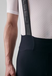 Shorts de cyclisme noirs avec des bretelles en mesh, présentant une texture lisse et une taille élastique. Le haut est en tissu léger et respirant à motif.