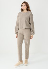 Beżowy sweter z teksturowanego dzianiny i spodnie o wąskim kroju, obie rzeczy o miękkim, lekkim wyglądzie. W zestawieniu z jasnobeżowymi trampkami.